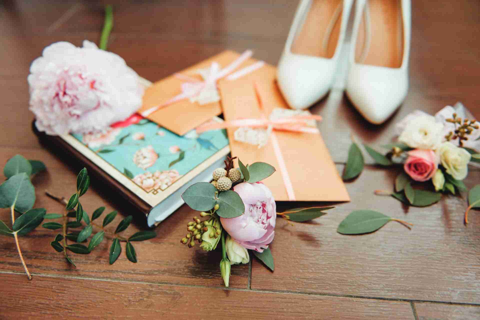 Wedding invitations, flowers, and white bridal shoes on wooden floor